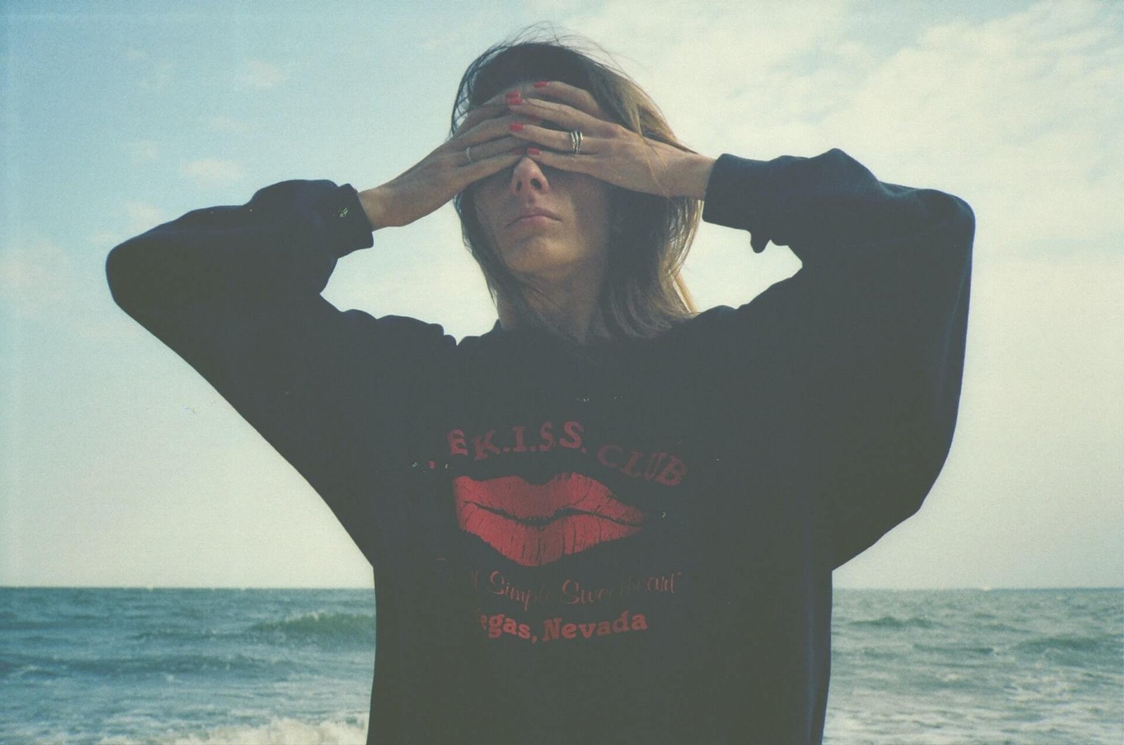 woman standing at beach with eyes covered with palms